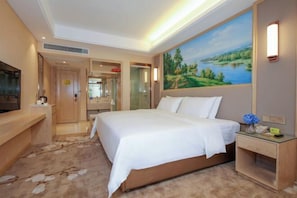 A hotel room with a large bed, a TV, a painting of a landscape, and a desk with a lamp. - Vienna Classic Hotel (Chongqing Bishan Aokang) (Chongqing)