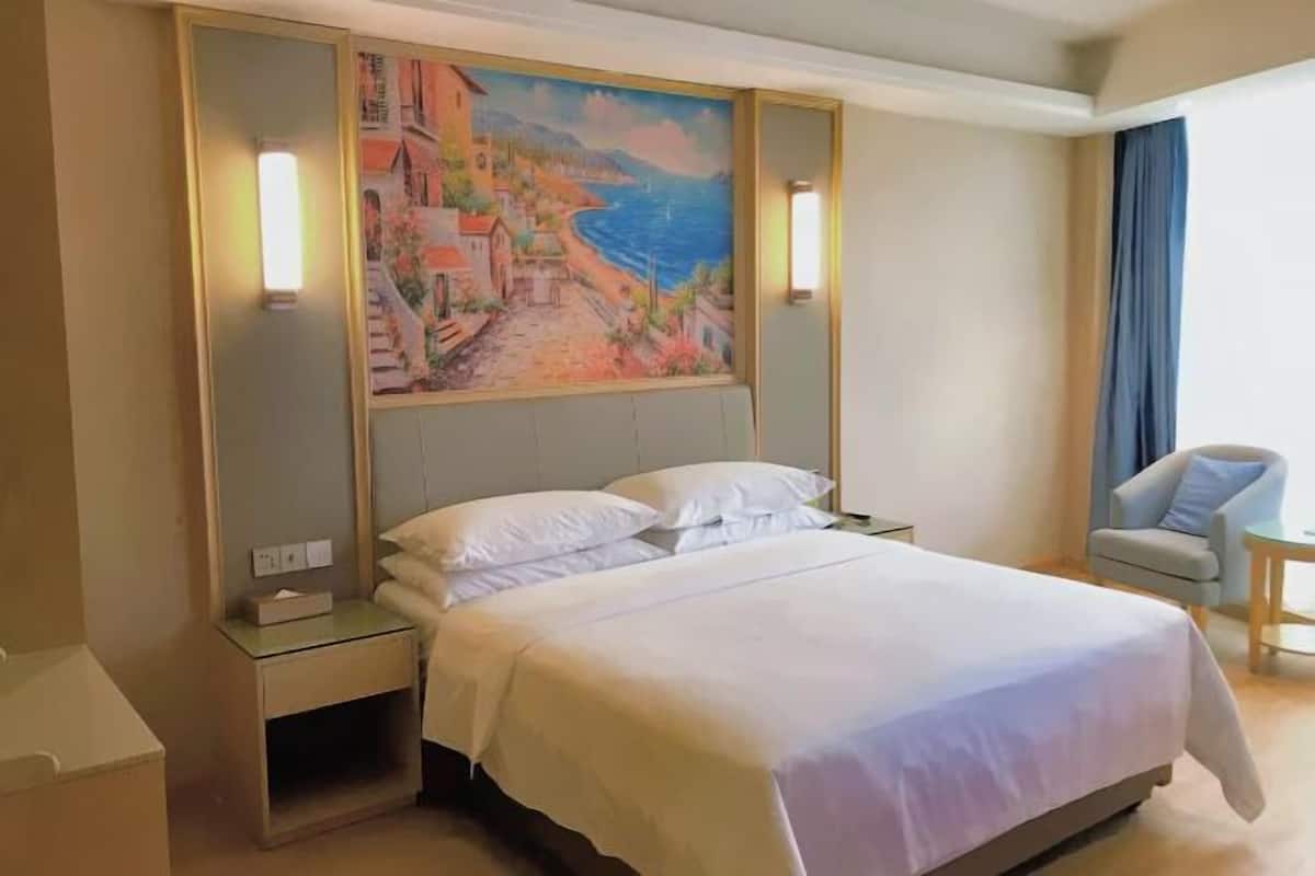 Una habitación de hotel con cama, dos mesitas de noche, un cuadro en la pared y una silla cerca de la ventana.