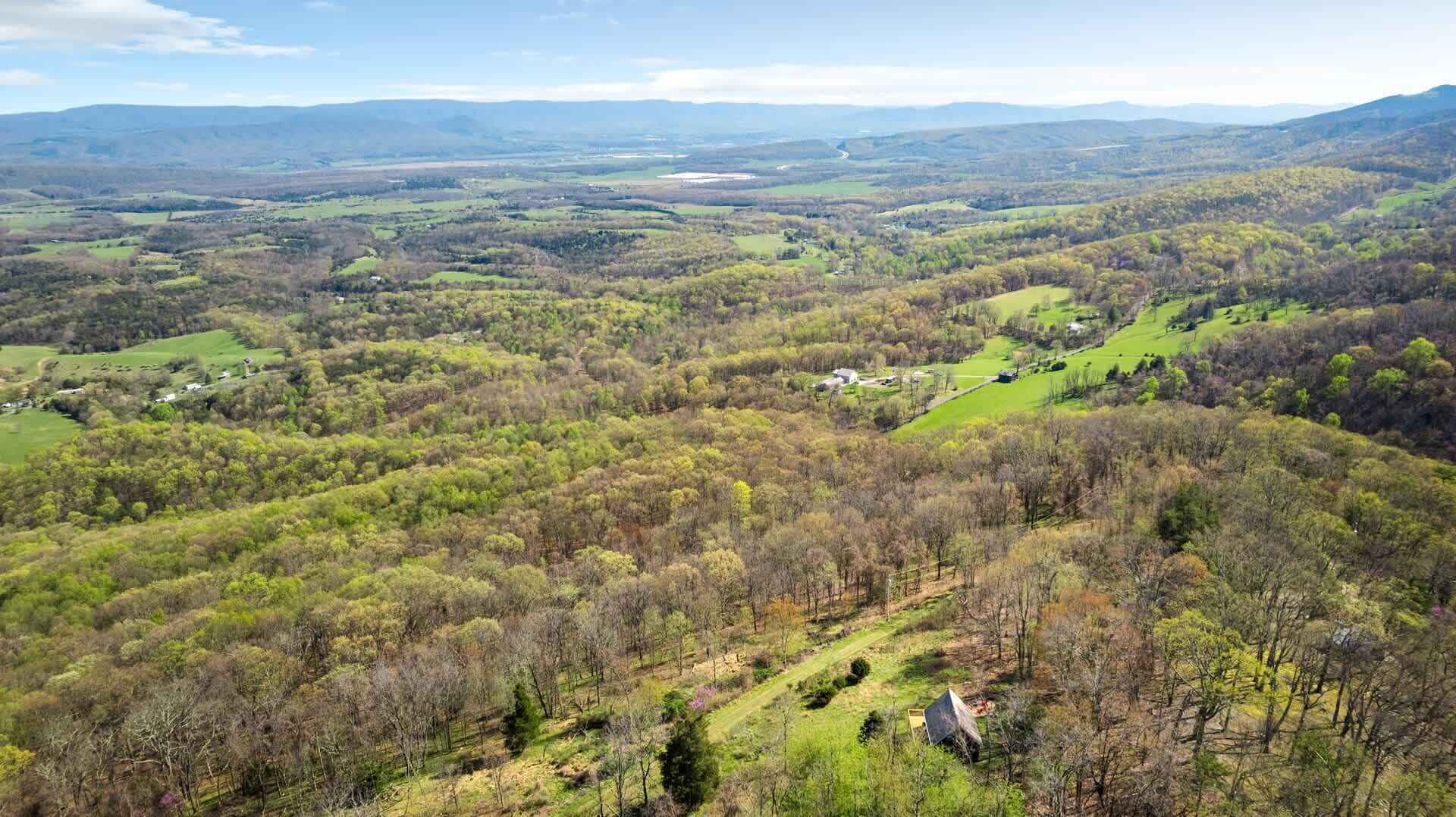 Una vista panoramica di un paesaggio rurale, con dolci colline, alberi sparsi e alcuni edifici.