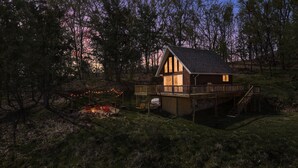 Une cabane dotée d’une terrasse, entourée d’arbres, et avec un foyer extérieur.