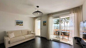 Una sala de estar moderna con un sofá, un comedor con mesa y sillas, y un balcón con vista al mar.