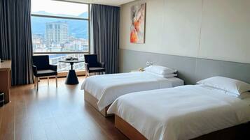 Habitación de hotel con dos camas, un escritorio, dos sillas, una mesita pequeña y un ventanal grande con vistas a la ciudad.