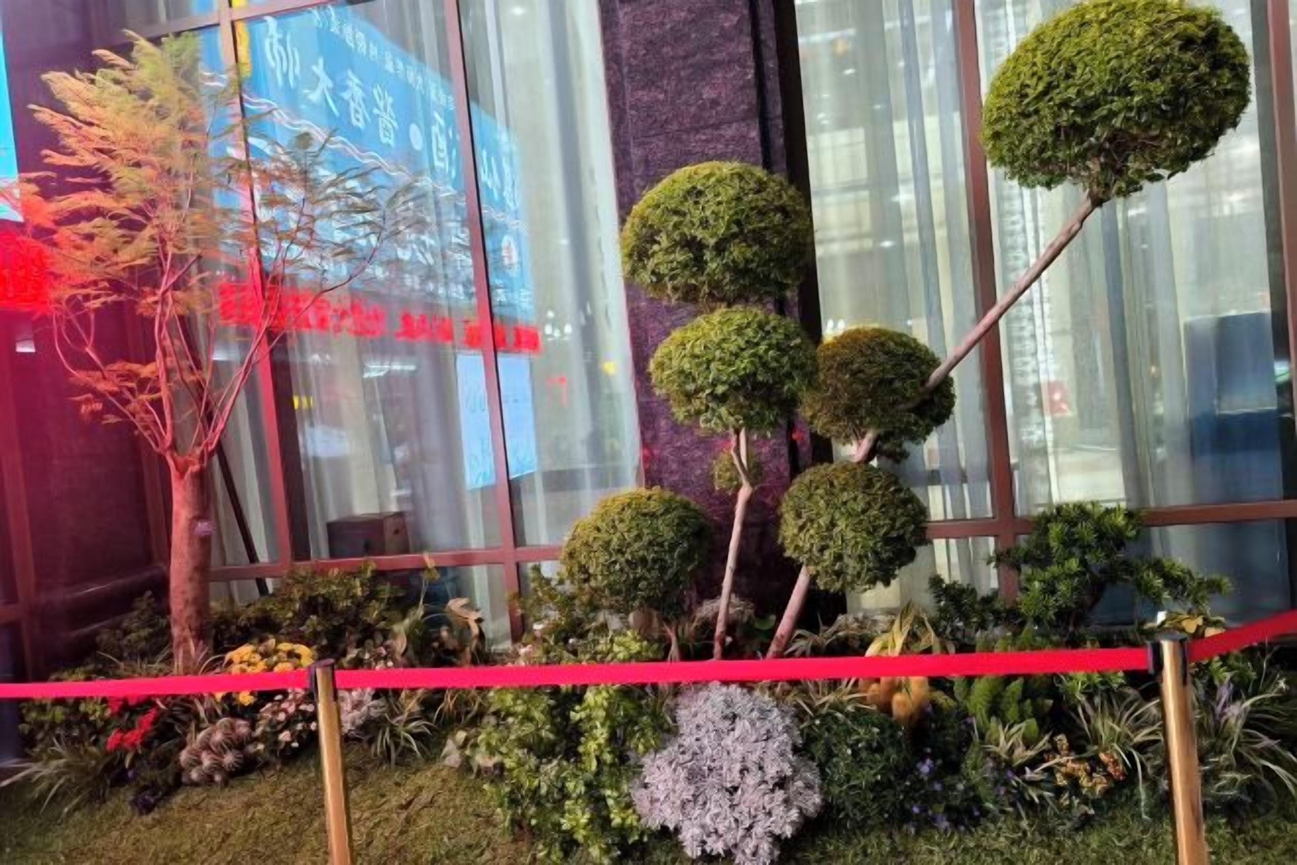 Un espace paysager agrémenté de diverses plantes taillées en formes géométriques et délimité par une barrière rouge.