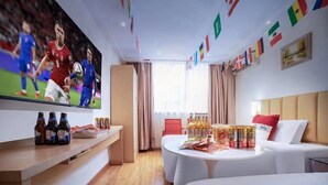 A hotel room with a television displaying a sports event, a round dining table with snacks, a sofa, and a bed. - Red Lantern Traders Hotel (Nanning)