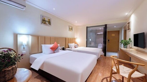 A hotel room with two beds, a desk, a chair, a television, and a plant. - Red Lantern Traders Hotel (Nanning)