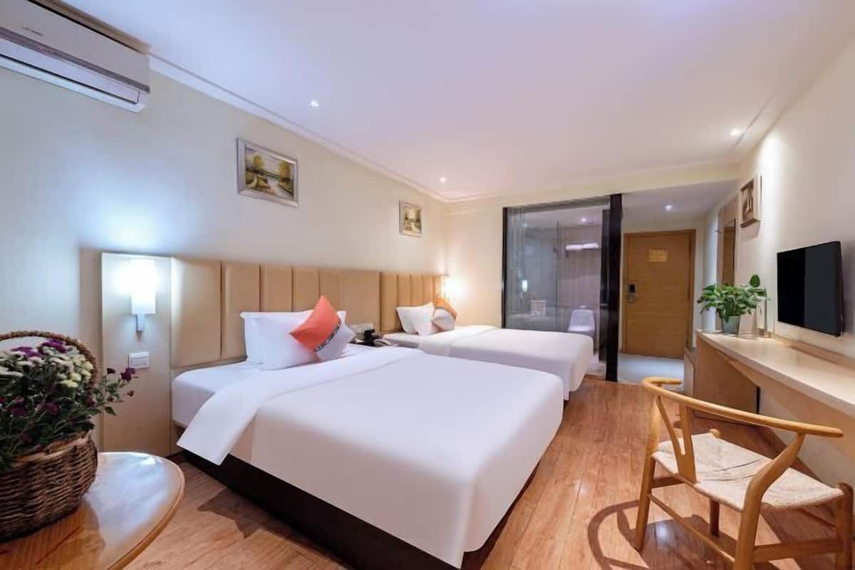 A hotel room with two beds, a desk, a chair, a television, and a plant.