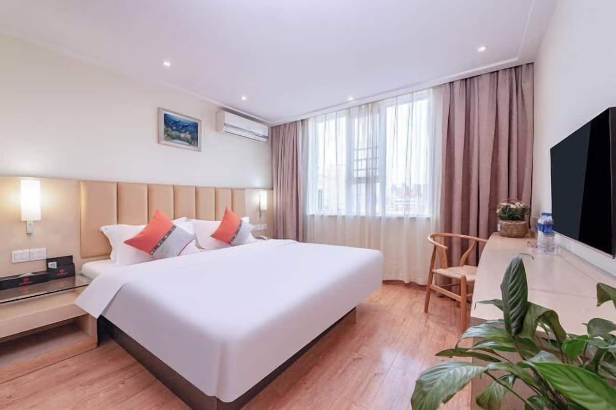 A hotel room with a bed, bedside table, TV, and a window with curtains.
