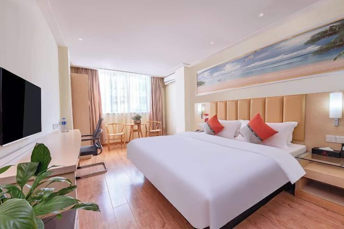 A hotel room with a large bed, a TV, a desk, and a painting on the wall.