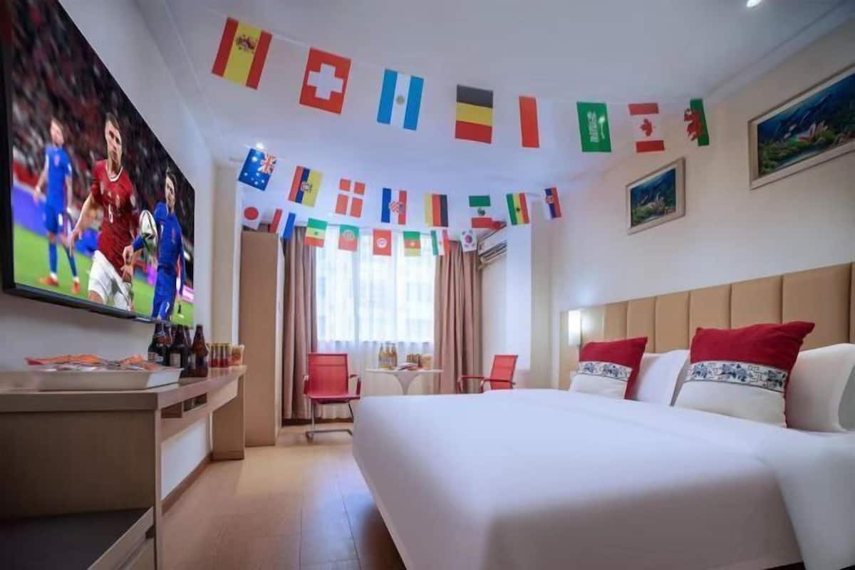 A hotel room with a large bed, a desk with a TV, and a window with curtains.