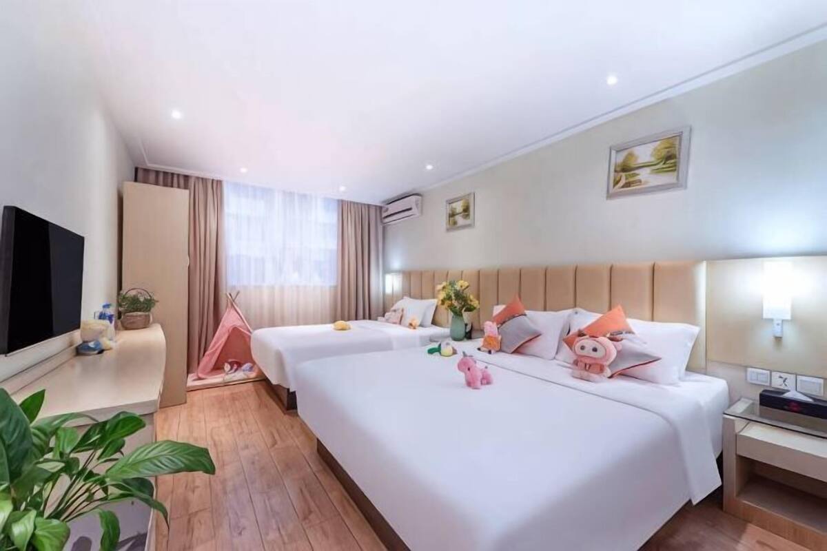 A hotel room with two beds, a TV, a desk, and a small window.