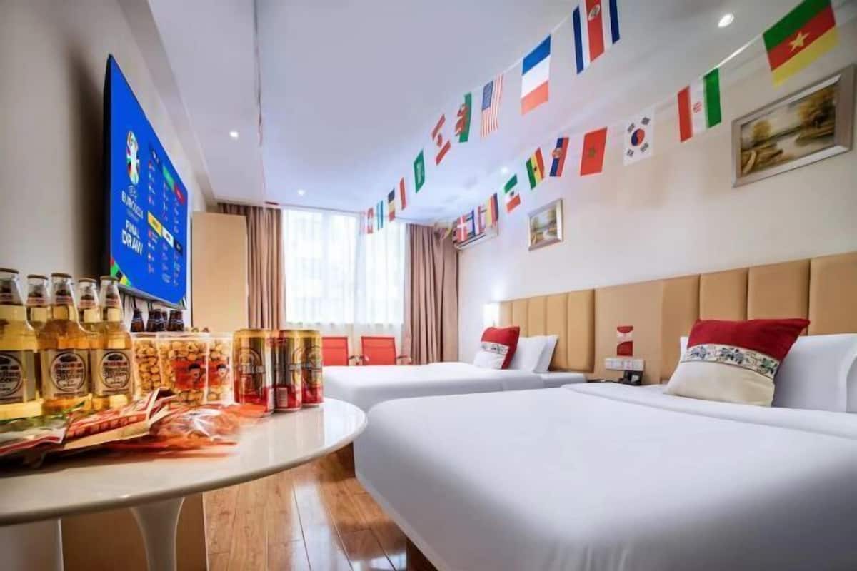 A hotel room with two beds, a TV, a table with snacks, and flags on the wall.