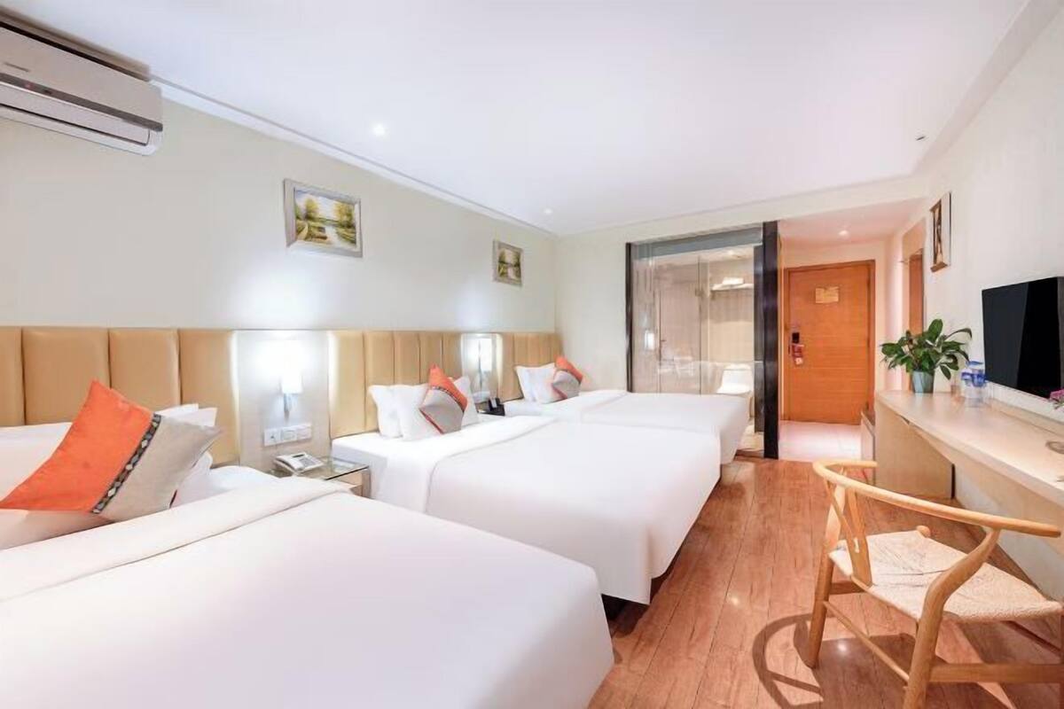 A hotel room with three beds, a wooden floor, a desk with a chair, and a television.