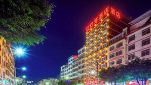 A multi-story hotel with illuminated signage, a street view with parked cars, and various storefronts. - Red Lantern Traders Hotel (Nanning)