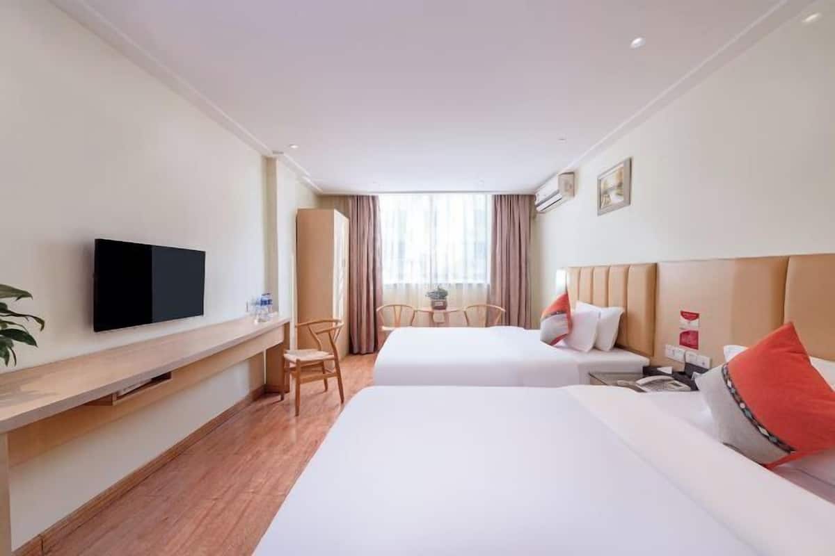 A hotel room with two beds, a TV, a desk, and a window with curtains.