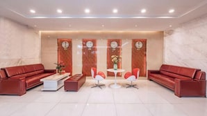 A modern lobby with red leather sofas, a coffee table, and two white chairs around a small table. - Red Lantern Traders Hotel (Nanning)