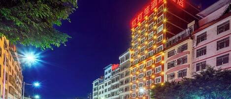 Un hotel de varios pisos con señalización iluminada, vista de la calle con vehículos y cielo nocturno despejado.