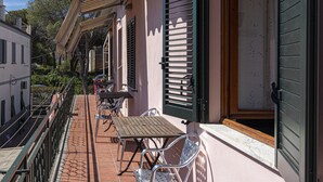 Un balcón con mobiliario exterior, incluyendo mesas y sillas, da a una calle con edificios.