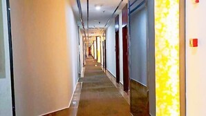 A long, narrow hotel corridor with a patterned carpet, doors on both sides, and a bright light fixture on the right wall. - Pinyi Hotel (Hefei Fanhua Avenue Zhonghuancheng) (Hefei)