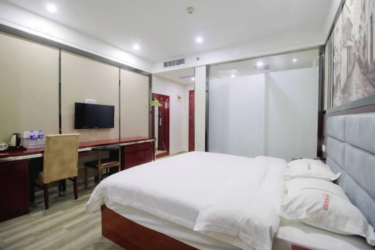 A hotel room with a bed, a desk, a chair, a television, and a door.