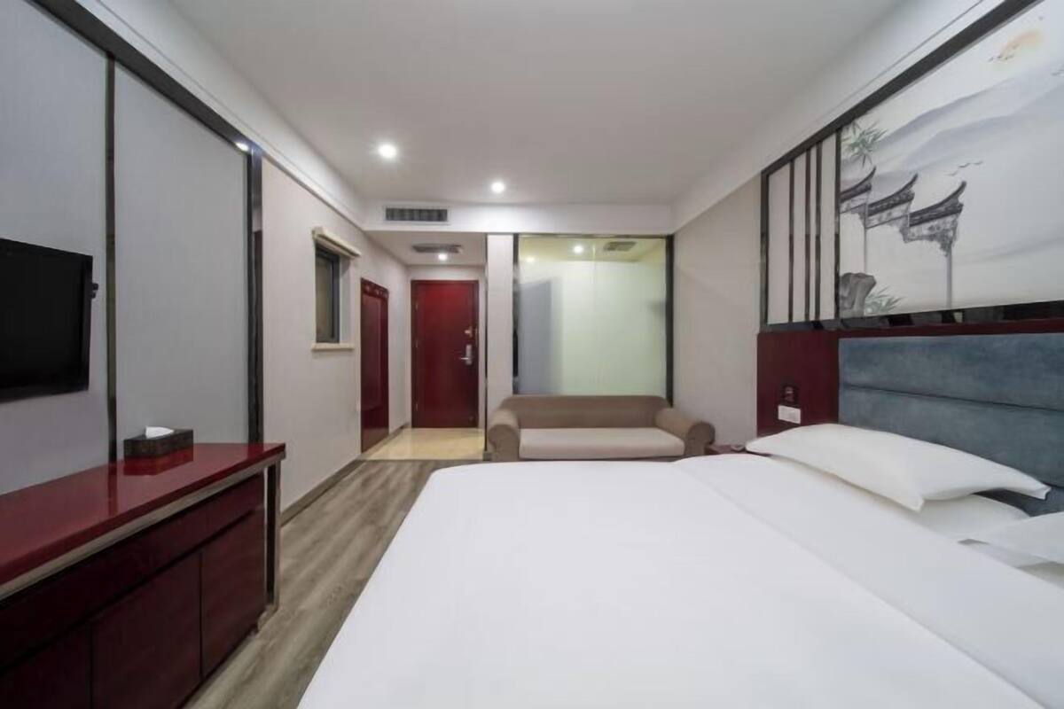 A hotel room with a bed, a TV, a desk, and a painting on the wall.