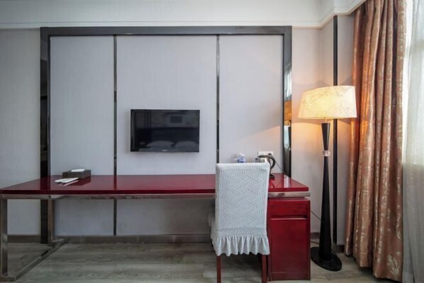 Une chambre d’hôtel avec un bureau rouge, un téléviseur fixé au mur, une lampe et une chaise recouverte d’une housse blanche.