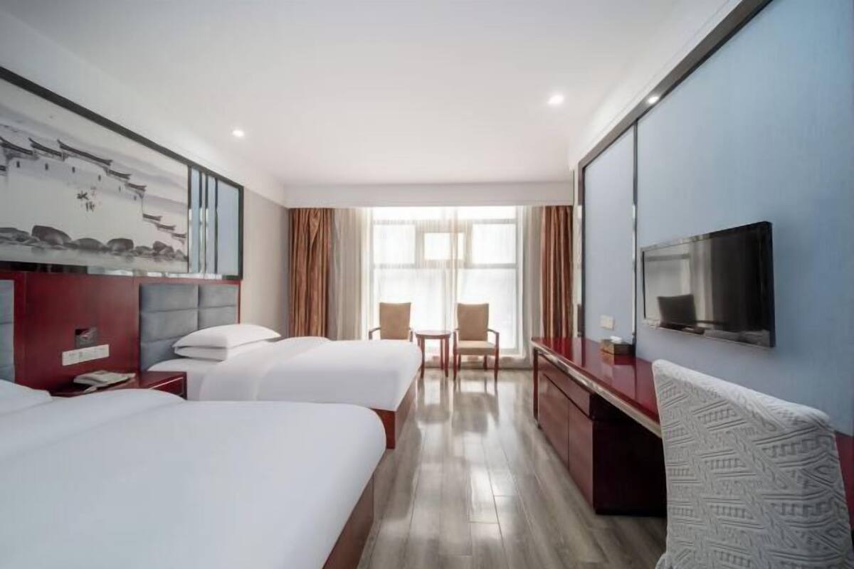 A hotel room with two beds, a desk, a TV, and a large window.