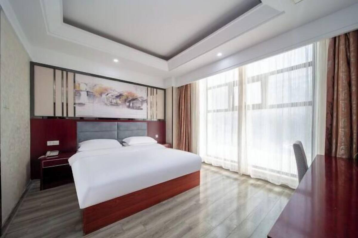 A hotel room with a large bed, a desk, and a painting on the wall.