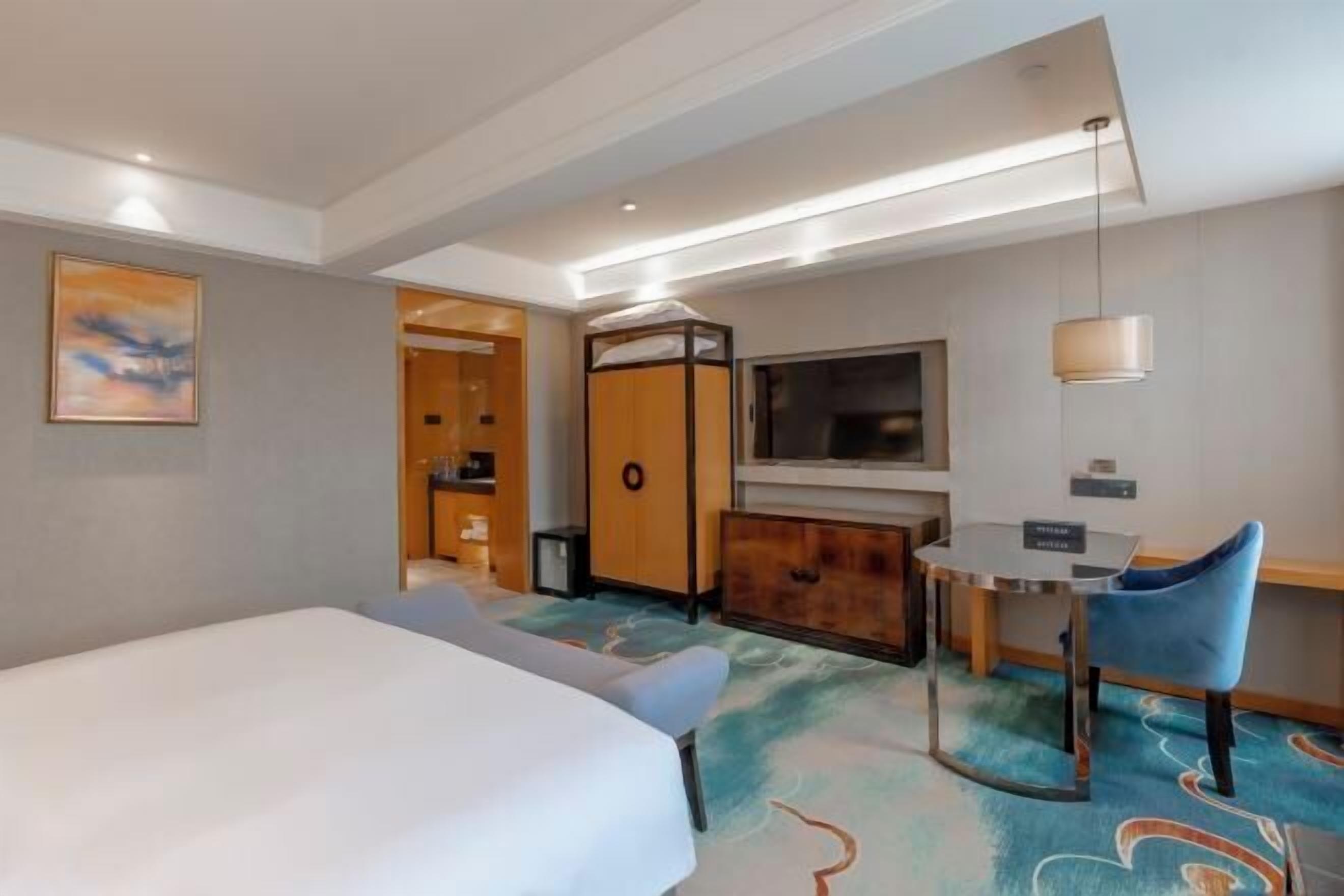 A hotel room with a bed, a desk, a chair, a TV, and a cabinet.