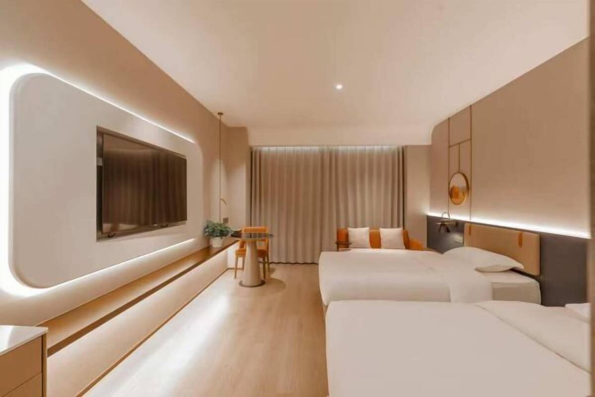 A hotel room with two beds, a TV, a desk, and a window with curtains.