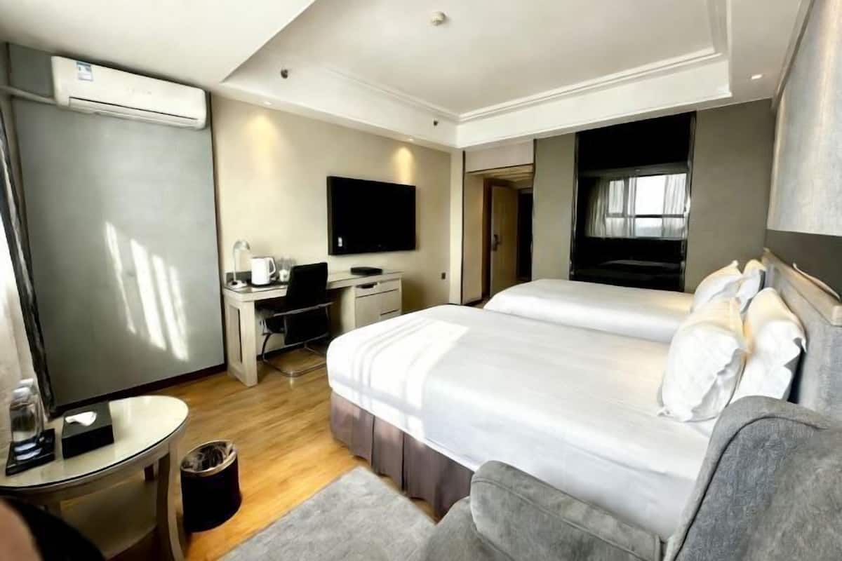 A hotel room with a bed, a desk, a chair, a TV, and an air conditioning unit.