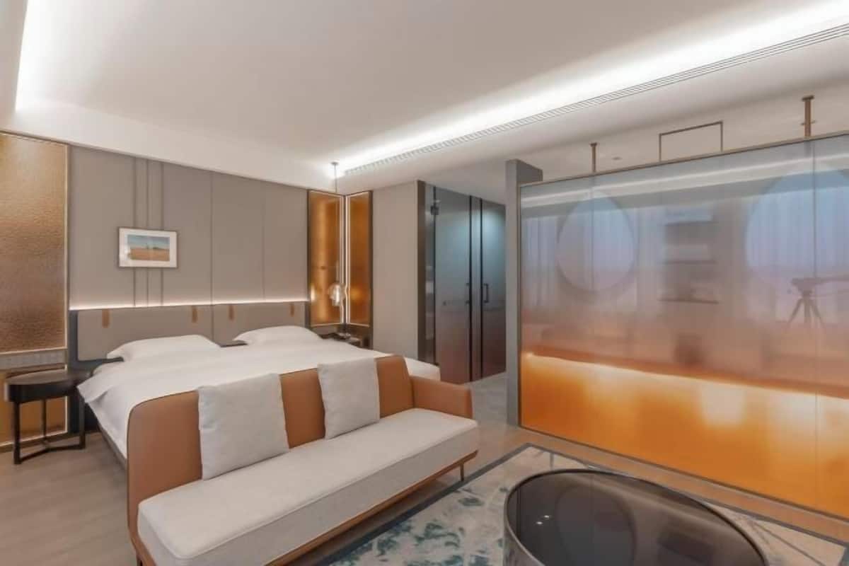 A modern hotel room with a bed, a sofa, a desk, and a large window.