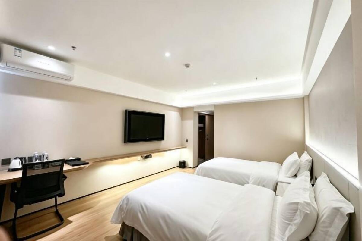 A hotel room with a bed, a desk, a chair, a television, and an air conditioning unit.