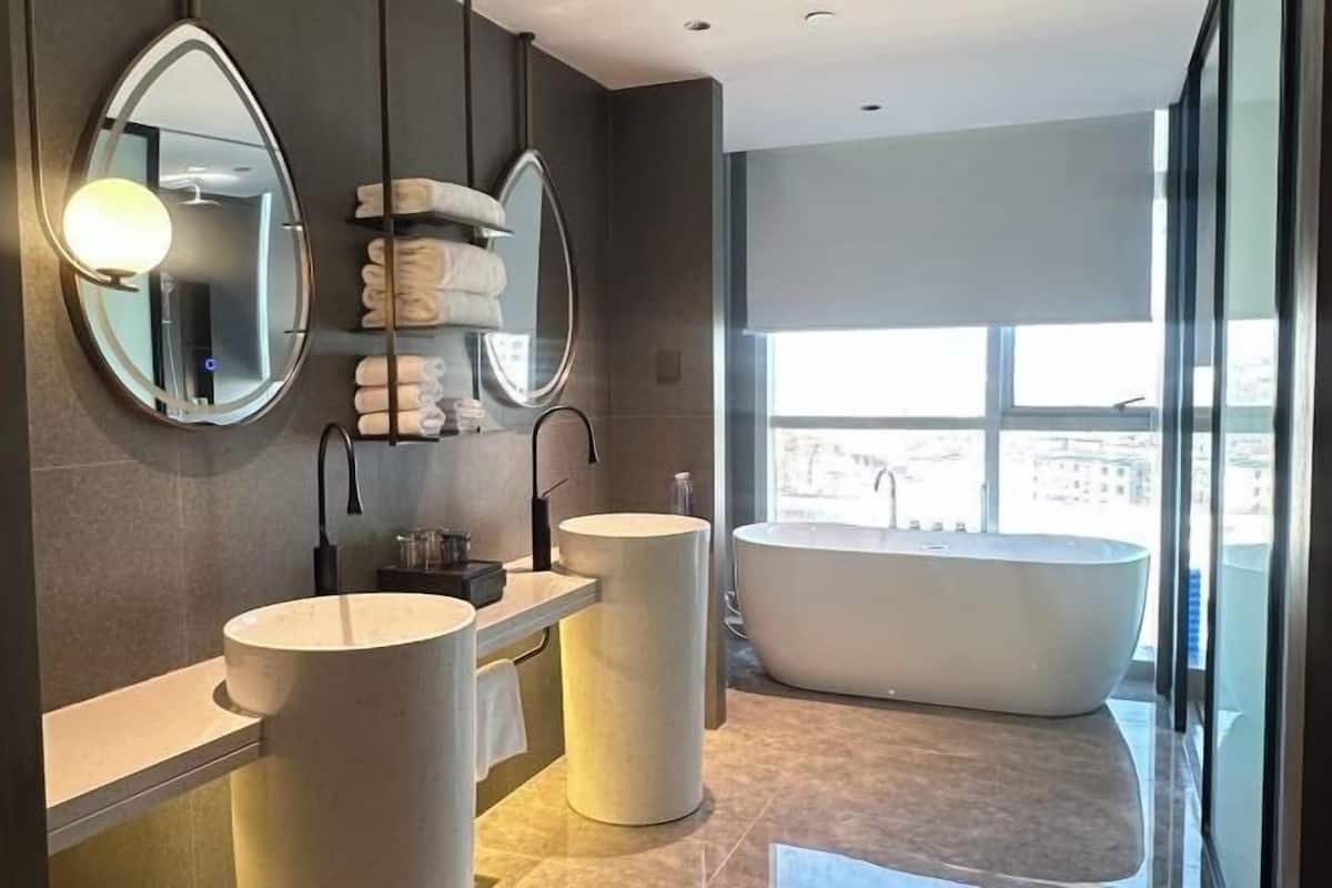 A modern bathroom with two sinks, a large bathtub, and a mirror with a light fixture.