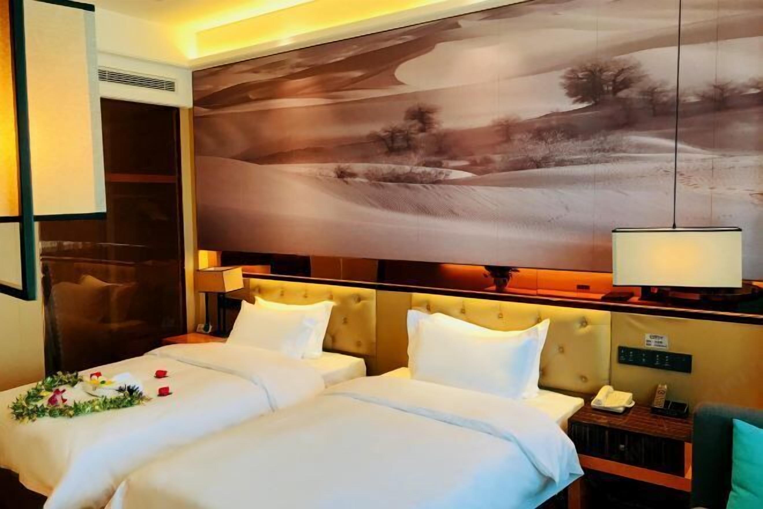 A hotel room with two beds, a large painting on the wall, a bedside table with a lamp, and a view of a landscape.