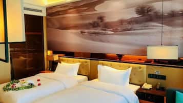 A hotel room with two beds, a large painting on the wall, a bedside table with a lamp, and a view of a landscape.