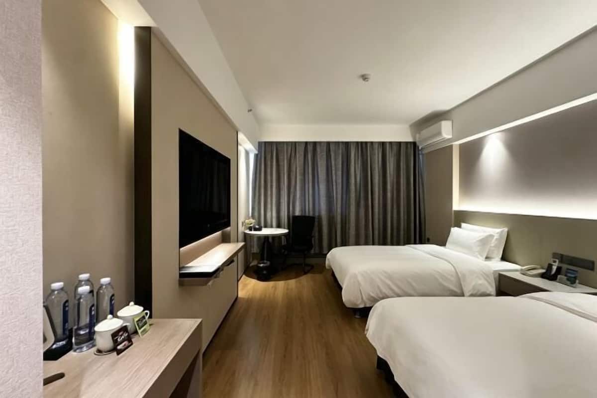 A hotel room with two beds, a desk with a chair, a TV, and a small table with a chair.
