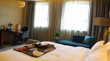 A hotel room with a bed, a desk, a chair, a sofa, and a window with curtains.