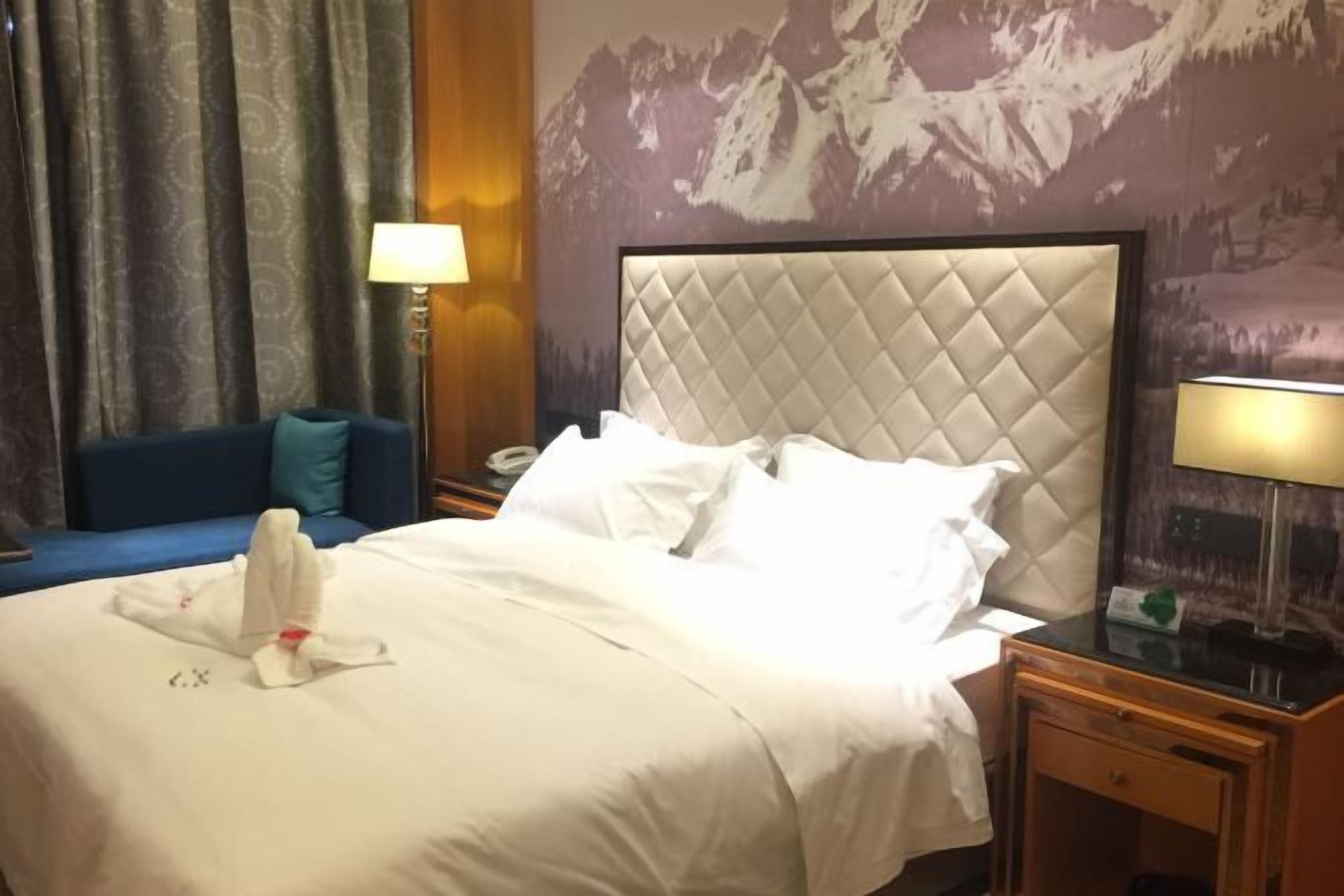 Et hotelværelse med en stor seng, en blå sofa, et natbord med en lampe og en væg med et bjergmaleri.