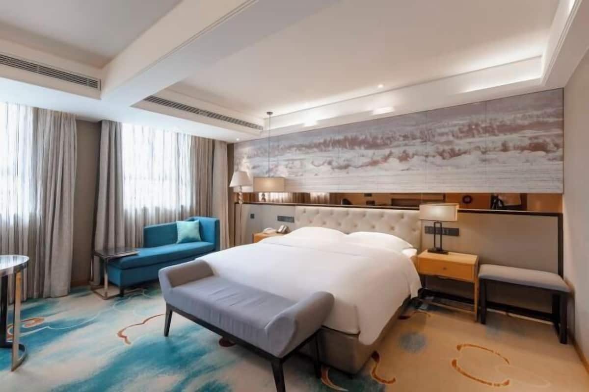 A hotel room with a large bed, a sofa, a desk, and a large painting on the wall.