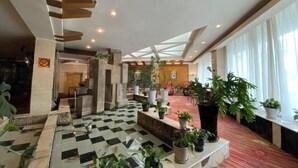 Un hall d’hôtel avec un sol à carreaux, un escalier et diverses plantes en pot.