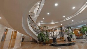 Un hall d’entrée spacieux, agrémenté d’un escalier en colimaçon, d’une fontaine centrale et de plantes en pot.