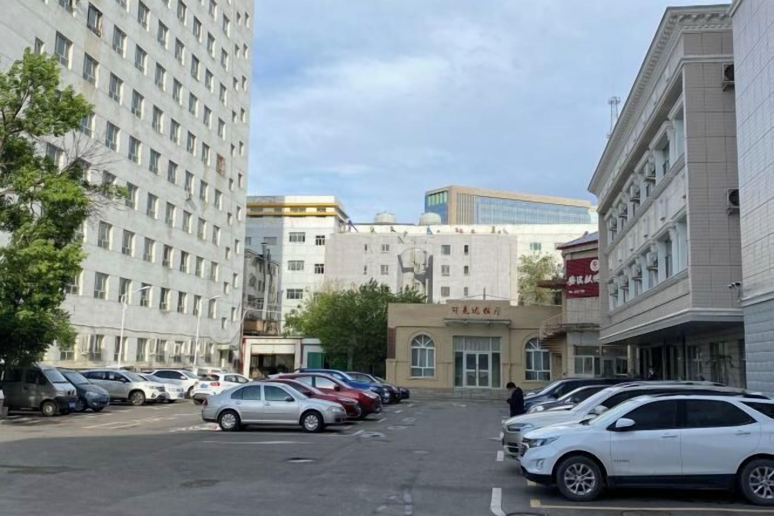 Un estacionamiento con varios autos, un edificio con un letrero que dice 'TOURIST HOTEL' y un edificio alto al fondo.