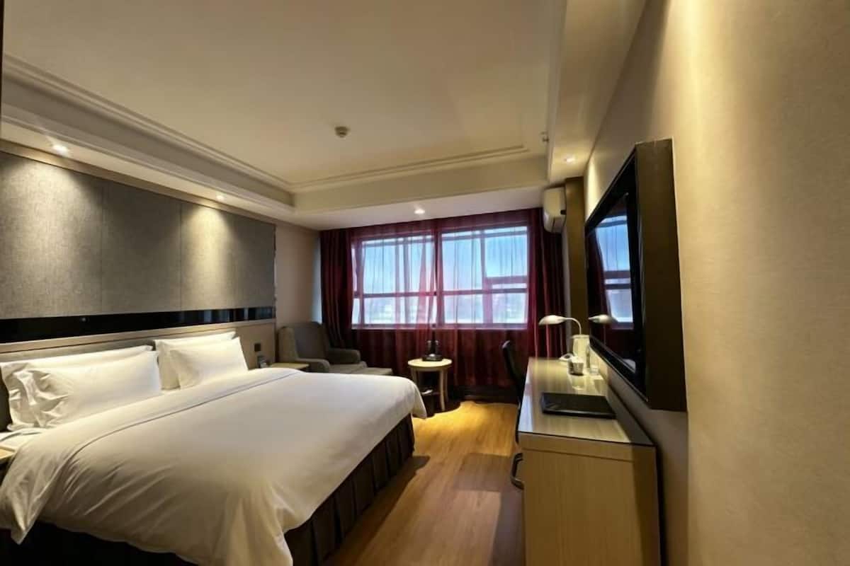 A hotel room with a large bed, a desk with a chair, a television, and a window with curtains.