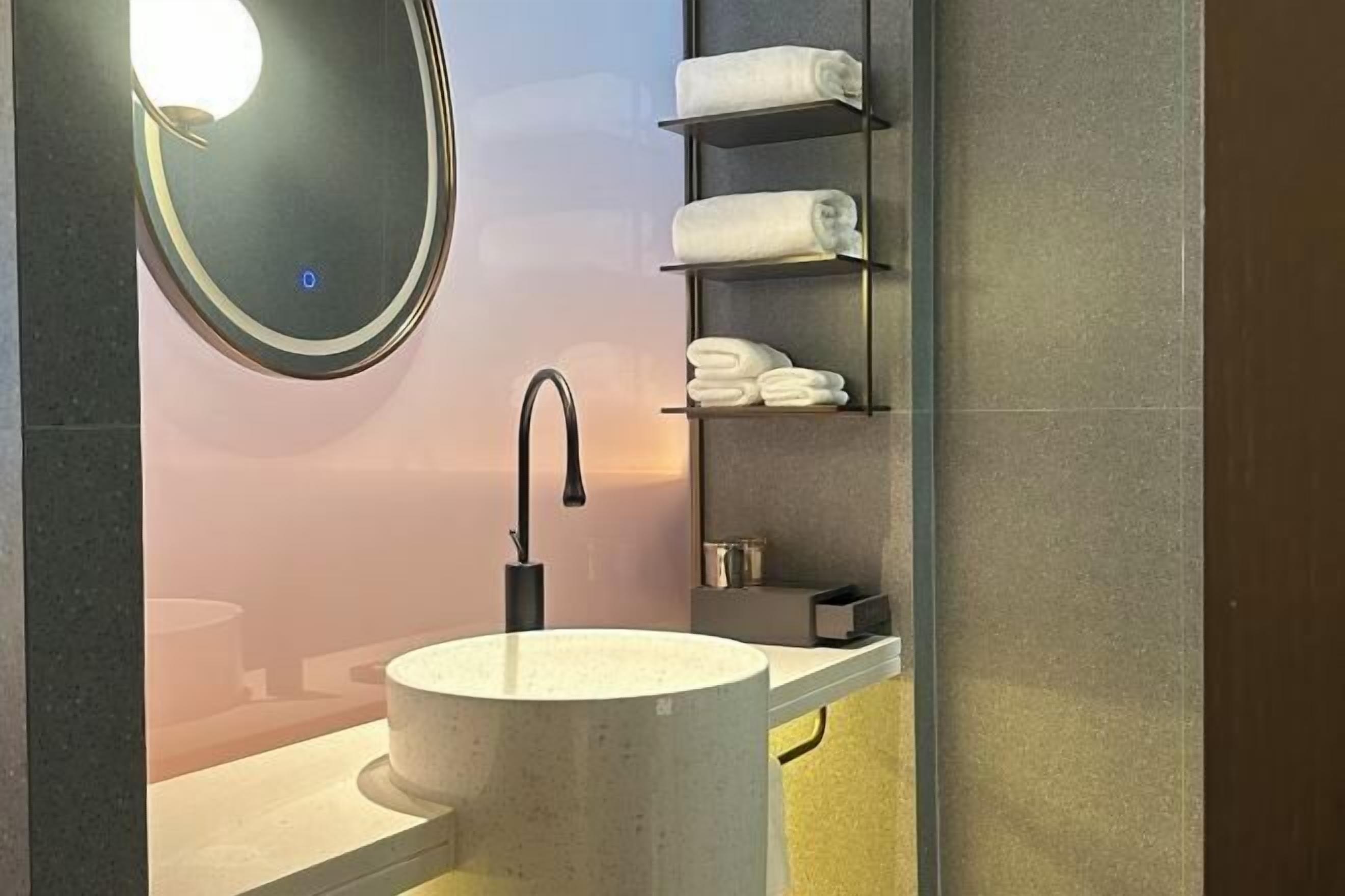 Un bagno moderno con uno specchio rotondo, un lavandino e scaffali con asciugamani piegati.