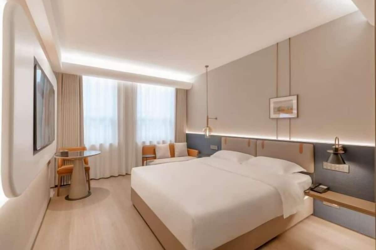 A modern hotel room with a large bed, bedside tables, a desk, and a view of the city.