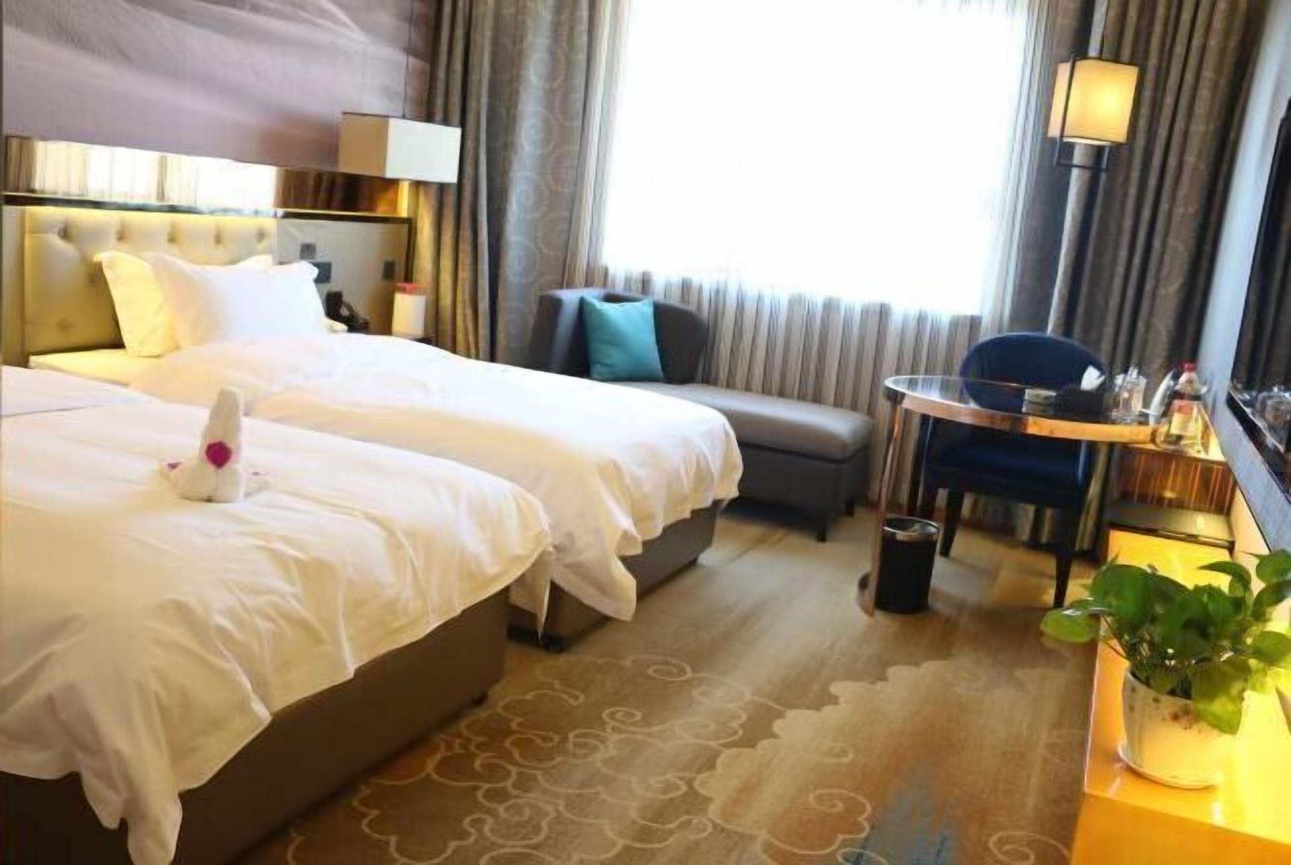 A hotel room with two beds, a sofa, a small table, and a potted plant.