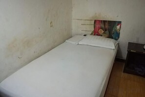 Una cama individual con ropa blanca en una habitación con paredes lisas y suelo de madera.