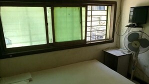 A single bed in a room with a window, a small table, and a wall-mounted fan. - Pingan Inn (Jingmen)