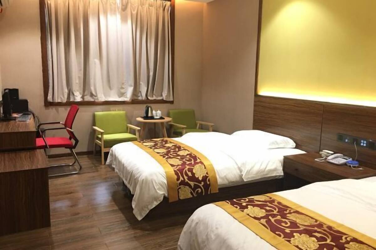 Ein Hotelzimmer mit zwei Betten, einem Schreibtisch, einem Stuhl, einem kleinen Tisch und einem Fenster mit Vorhängen.