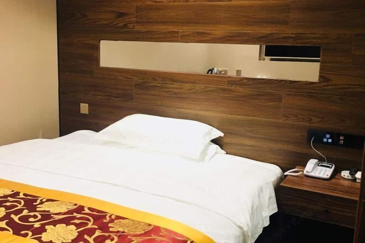 Ein Hotelzimmer mit einem Holzkopfteil, einem Bett mit weißer Bettwäsche, einem Telefon auf einem Nachttisch und einer kleinen Ablage mit Toilettenartikeln.